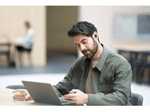 Charger l&#39;image dans la galerie, Un homme utilisant un ordinateur portable, tenant un téléphone et un verre d&#39;eau sur un bureau.
