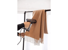 Charger l&#39;image dans la galerie, Une personne utilise un défroisseur à main sur une écharpe beige suspendue à un support noir.
