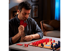 Charger l&#39;image dans la galerie, Un homme tenant des cartes, regardant un jeu de société avec des pièces rouges et bleues.
