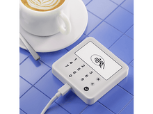 Charger l&#39;image dans la galerie, Une tasse à café blanche sur une soucoupe, un lecteur de carte et un câble sur des carreaux bleus.
