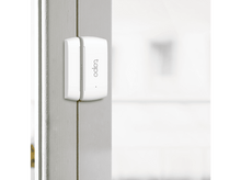 Charger l&#39;image dans la galerie, Un capteur de porte Tapo blanc monté sur un cadre de porte blanc, avec un arrière-plan flou.
