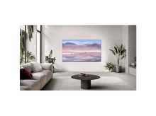 Charger l&#39;image dans la galerie, Salon avec une grande télévision montrant un paysage. Un canapé, des plantes et une table ronde sont visibles.
