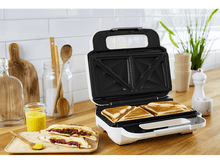 Charger l&#39;image dans la galerie, Un appareil à sandwich blanc et noir avec des sandwichs cuits et des ingrédients sur un comptoir.
