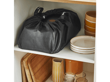 Charger l&#39;image dans la galerie, Un sac noir à l&#39;intérieur d&#39;une étagère de placard blanche, avec des planches à découper et des assiettes à proximité.
