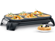 Charger l&#39;image dans la galerie, Gril à crêpes avec crêpes cuites, certaines garnies de saumon et de caviar. Une pile de crêpes.
