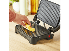 Charger l&#39;image dans la galerie, Une personne plaçant un morceau de pain sur un grill noir avec bouton rouge.
