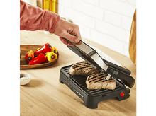 Charger l&#39;image dans la galerie, Personne grillant des steaks sur un grill noir. Le grill est sur un comptoir en bois avec des poivrons et du sel à proximité.
