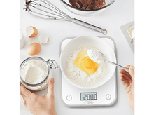 Charger l'image dans la galerie, Vue aérienne : œuf dans la farine sur une balance, pot de farine et mains sur une surface blanche.
