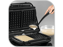 Charger l&#39;image dans la galerie, Une personne verse de la pâte d&#39;une louche dans un gaufrier. Une gaufre est en train de cuire.
