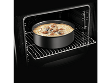 Charger l&#39;image dans la galerie, Pizza dans un moule noir à l&#39;intérieur d&#39;un four. Le four est sombre avec une grille métallique. La pizza est visible.
