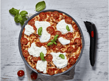 Charger l&#39;image dans la galerie, Pizza dans une poêle avec tomates, mozzarella et basilic, à côté d&#39;un coupe-pizza noir.
