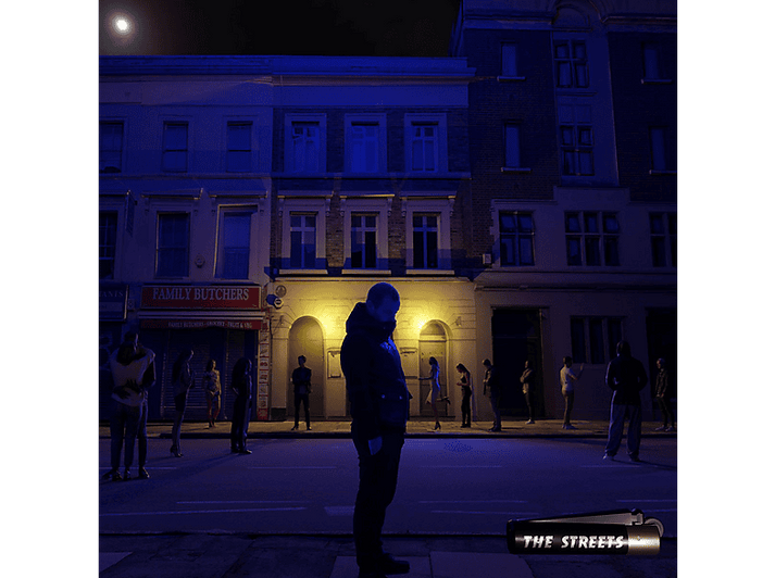 Scène de nuit avec des bâtiments et des gens. Un homme au premier plan. Panneau 'The Streets'.