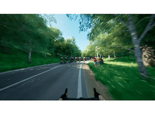 Charger l&#39;image dans la galerie, Des cyclistes courent sur une route bordée d&#39;arbres avec des spectateurs et un ciel clair.
