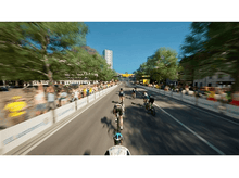 Charger l&#39;image dans la galerie, Cyclistes dans une course sur une route de ville avec des spectateurs et de grands bâtiments.
