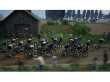 Charger l&#39;image dans la galerie, Des cyclistes courent sur une route avec des spectateurs et un petit bâtiment.
