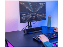 Charger l&#39;image dans la galerie, Un joueur jouant à un jeu de course sur un moniteur, avec un clavier, des haut-parleurs et une bouteille d&#39;eau.
