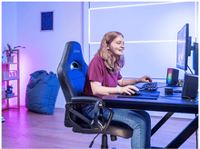 Charger l'image dans la galerie, Une jeune femme souriante joue sur un bureau. Un écran et des haut-parleurs sont visibles.
