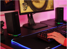 Charger l&#39;image dans la galerie, Haut-parleurs, moniteur et clavier sur un bureau noir, avec un effet d&#39;éclairage coloré.
