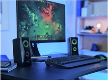 Charger l&#39;image dans la galerie, Haut-parleurs noirs avec lumières RVB, un moniteur affichant un jeu, clavier et souris sur un bureau.
