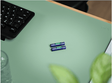 Charger l&#39;image dans la galerie, Deux piles AA, étiquettes bleues et vertes, sur un tapis de bureau vert, près d&#39;un clavier noir.
