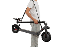 Charger l'image dans la galerie, Une personne tenant une trottinette noire pliée par une sangle. La trottinette est grise et noire.
