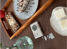 Charger l&#39;image dans la galerie, Un appareil photo, un gâteau, des noix et une boisson sur un plateau en bois sur une table.
